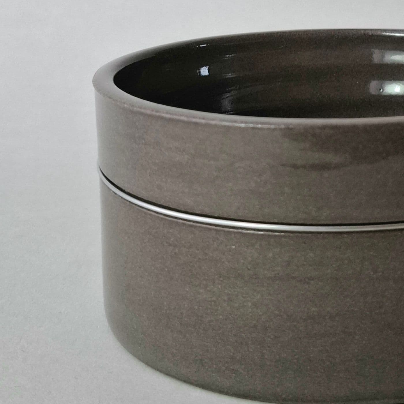 A cylindrical dark gray ceramic bowl with a smooth, glossy finish. The vessel features straight vertical walls and a flat base, presenting a uniform dark gray color throughout the exterior surface with a subtle horizontal seam line.