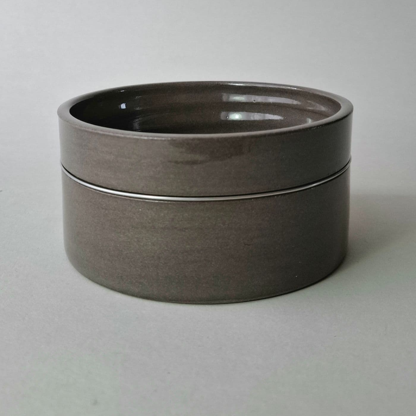A cylindrical dark gray ceramic bowl with a smooth, glossy finish. The vessel features straight vertical walls and a flat base, presenting a uniform dark gray color throughout the exterior surface with a subtle horizontal seam line.