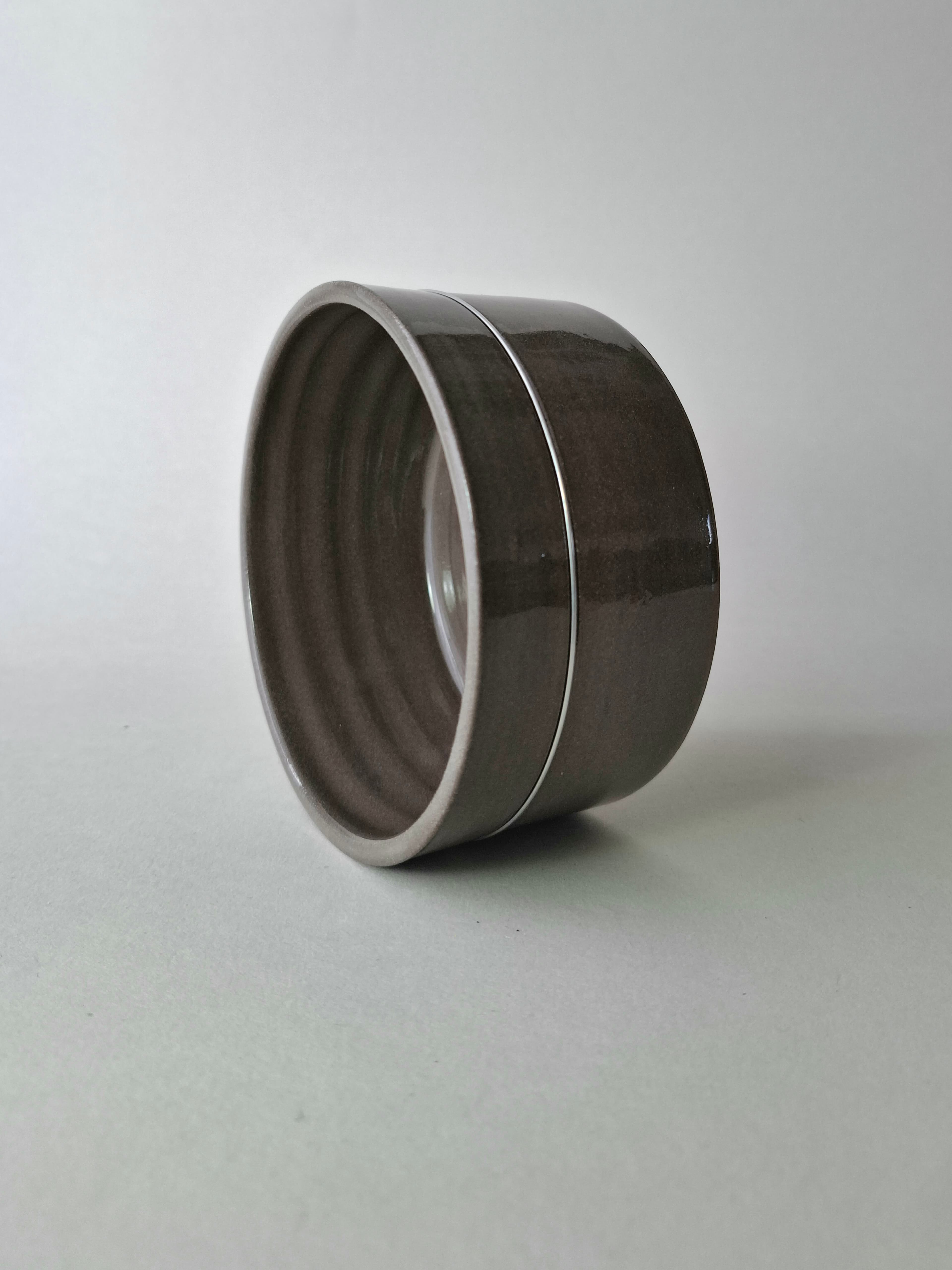 A cylindrical dark gray ceramic bowl with a smooth, glossy finish. The vessel features straight vertical walls and a flat base, presenting a uniform dark gray color throughout the exterior surface with a subtle horizontal seam line.